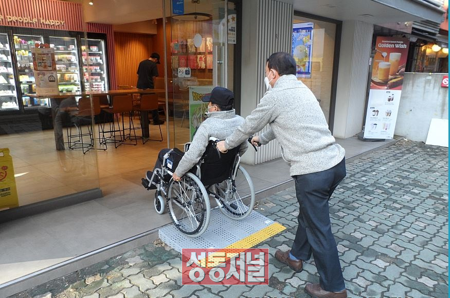 휠체어를 이용하는 주민이 경사로를 통해 가게 입구로 들어가고 있다.